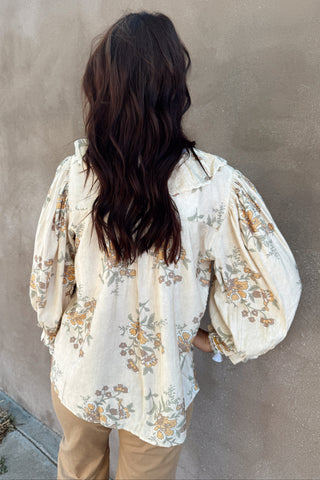 Person wearing a floral blouse against a plain wall
