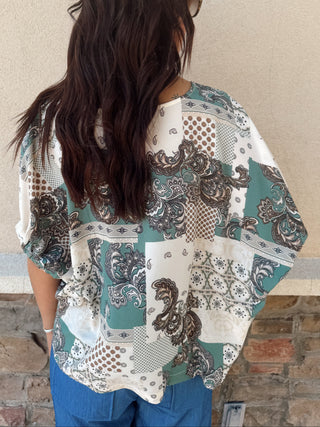 Woman wearing a patterned shirt against a beige wall.