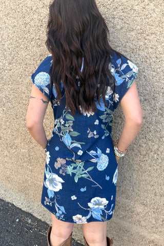 Person wearing a blue floral dress standing against a beige wall.