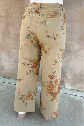 Person wearing floral pants and a red top against a beige wall.