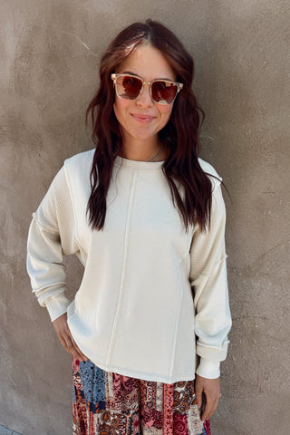 Woman wearing a white jacket and patterned pants against a gray wall