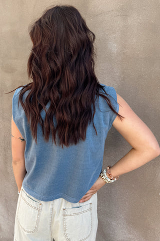 Person wearing a blue sleeveless top and light-colored pants against a plain wall.