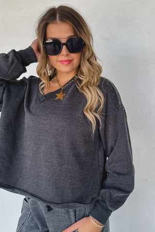 Woman wearing a dark gray sweatshirt and sunglasses against a plain background