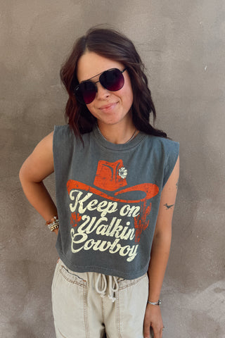 Woman wearing a sleeveless shirt with a cowboy graphic and text against a concrete wall.