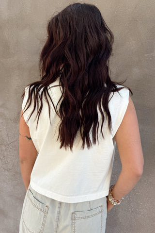 Person wearing a white sleeveless top and light-colored pants against a plain wall.