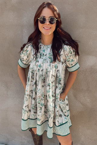 Woman wearing a floral dress and brown boots against a beige wall.