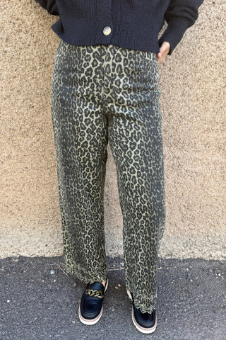 Person wearing leopard print pants and black shoes on a pavement.