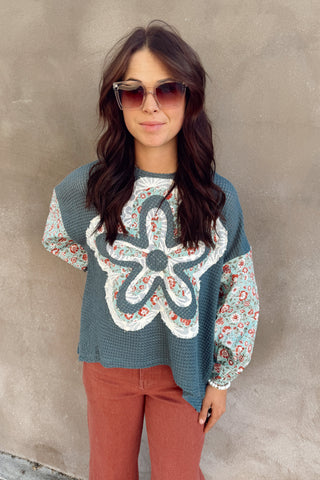Woman wearing a patterned sweater and sunglasses against a plain background