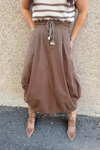 Person wearing a brown skirt and striped top against a textured wall.