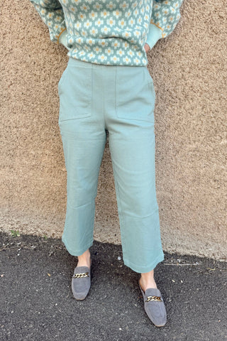 Person wearing a floral sweater and light blue pants standing against a beige wall.
