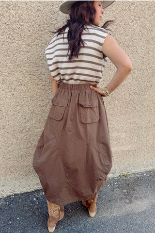 Woman wearing a striped shirt and brown skirt against a beige wall.