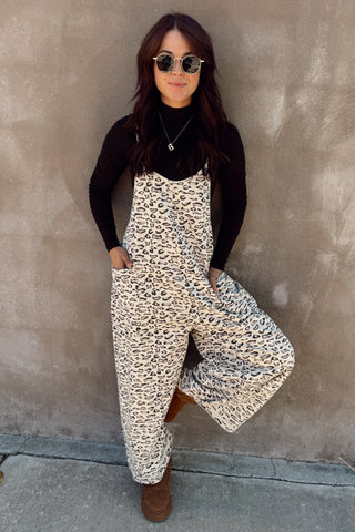 Person wearing a leopard print dress over a black top against a beige wall.
