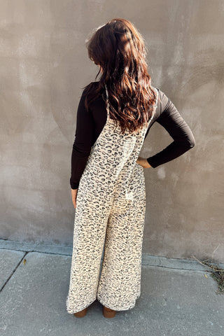 Person wearing a leopard print jumpsuit against a plain wall.
