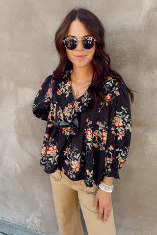 Woman wearing a floral blouse and sunglasses against a gray wall