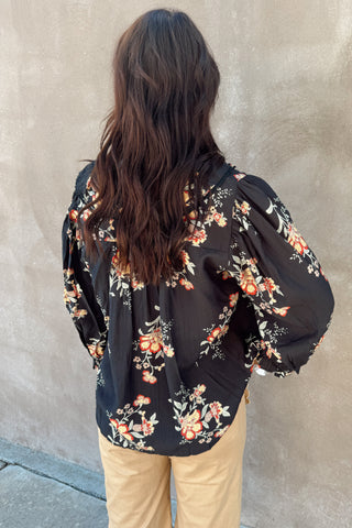 Person wearing a black floral blouse against a beige wall
