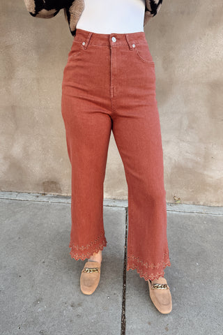 Person wearing high-waisted rust-colored jeans against a beige wall.