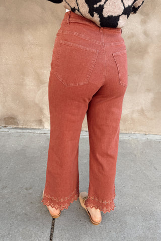 Person wearing rust-colored pants and a patterned sweater on a sidewalk.