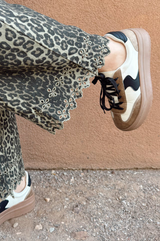 Person wearing leopard print pants and matching sneakers on a beige background