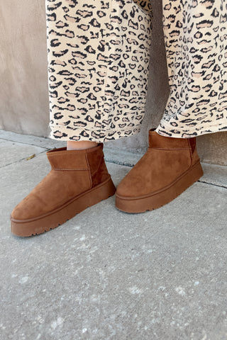 Brown suede boots worn with leopard print pants on a concrete surface.