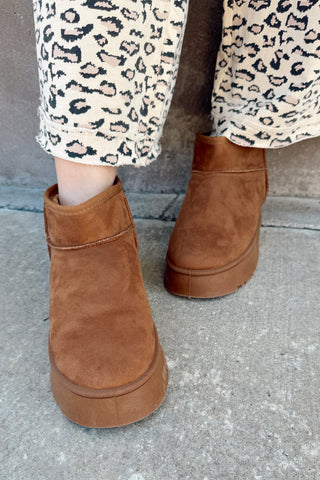 Brown suede ankle boots worn with leopard print pants on a concrete surface.