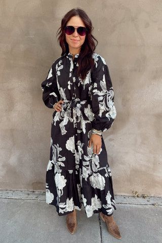 Woman wearing a black floral dress standing against a beige wall.