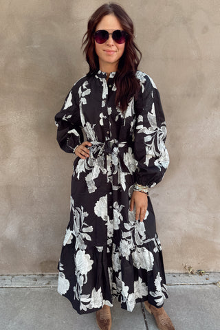 Woman wearing a black floral dress against a beige wall.