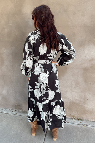 Woman wearing a black and white floral dress against a beige wall.