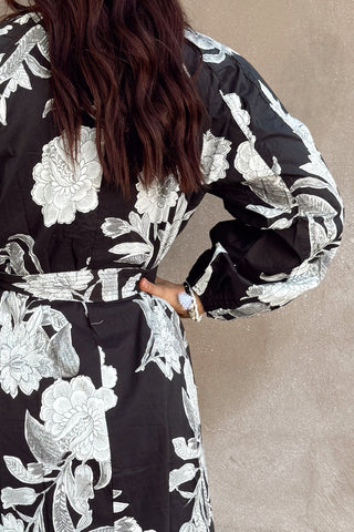 Woman wearing a black floral dress against a beige wall.