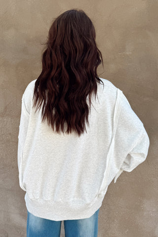 Person wearing a white oversized sweater and blue jeans against a beige wall