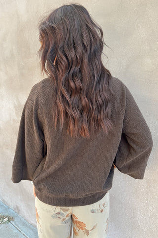 Person wearing a brown sweater against a beige wall