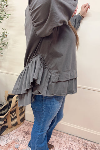 Person wearing a gray layered outfit with blue jeans in a room setting.