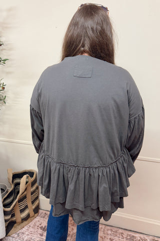 Person wearing a gray ruffled blouse in a home setting