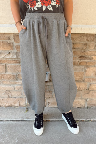 Person wearing gray sweatpants and black sneakers against a brick wall.