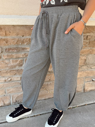 Person wearing gray sweatpants and black sneakers against a stone wall.