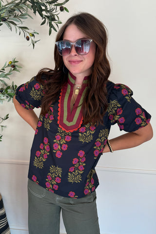 Woman wearing a floral blouse and sunglasses indoors with plants and a rug in the background