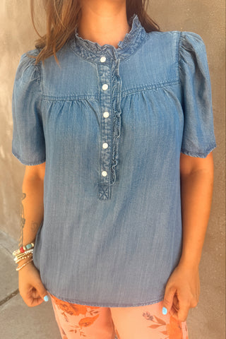 Person wearing a blue denim shirt with white buttons on a neutral background