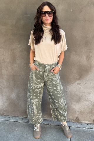 Person wearing a beige top and camouflage pants standing on a concrete floor.