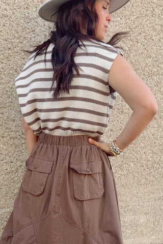 Woman wearing a striped shirt and brown skirt against a beige wall.