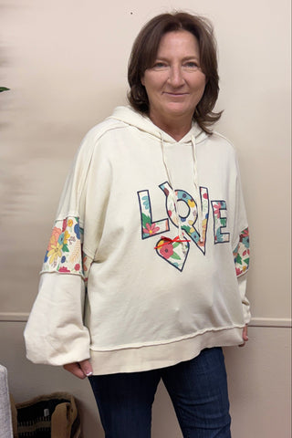 Person wearing a white sweatshirt with colorful designs indoors.