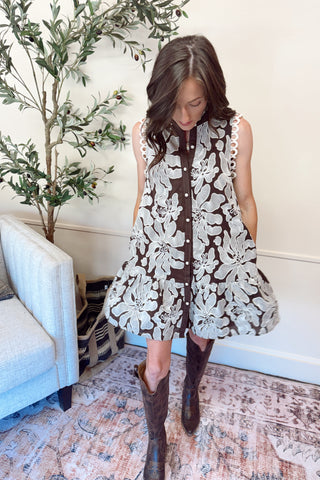 Woman wearing a brown and white floral dress with knee-high brown boots in a living room.