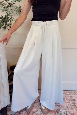 Person wearing white wide-leg pants and a black top in an indoor setting.