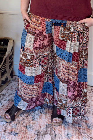 Woman wearing a burgundy t-shirt with a graphic design and patterned pants in a living room.