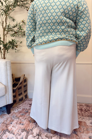 Person wearing a floral sweater and white pants in a living room setting.