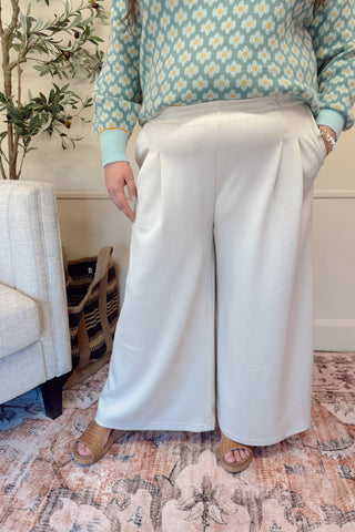 Person wearing a floral sweater and white pants sitting on a couch in a home setting.
