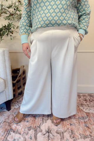 Person wearing a floral sweater and white pants sitting on a couch in a home setting.