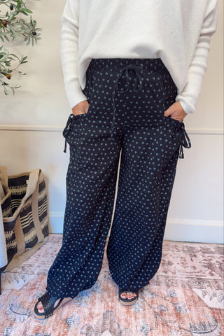 Person wearing navy polka dot pants with a white top in a room with a plant and rug.
