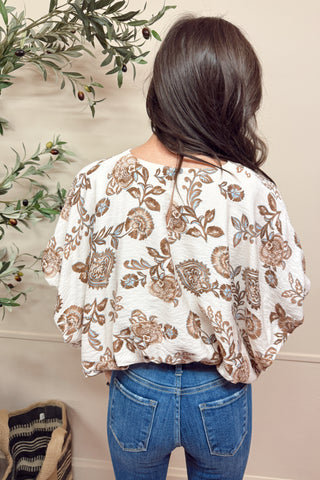 Woman wearing a floral blouse and blue jeans with a decorative background