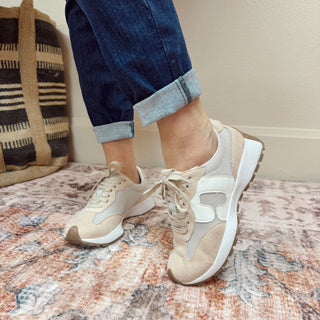 Person wearing beige sneakers on a patterned rug with a neutral background