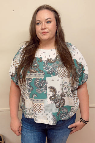 Woman wearing a patterned blouse and jeans against a plain background