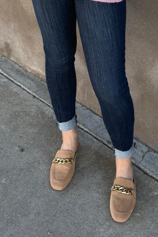 Person wearing dark blue jeans and brown loafers with gold chains on a concrete surface.